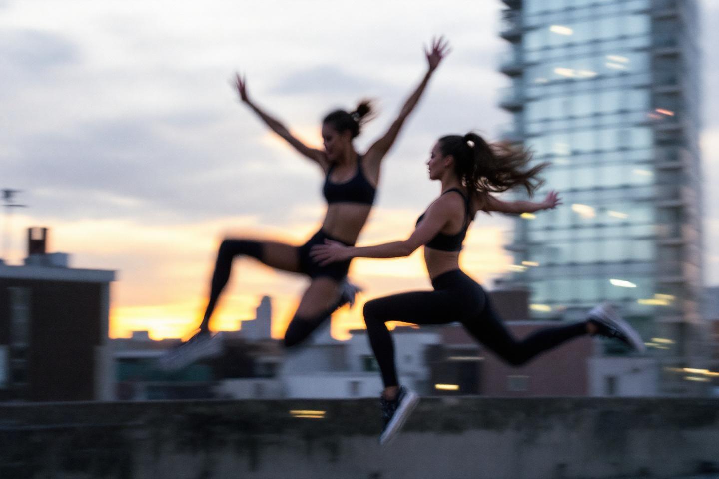 Deux silhouettes féminines sautant sur un toit au coucher du soleil