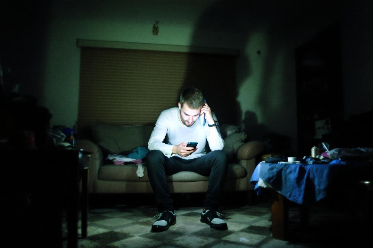 Un homme seul dans une pièce sombre, absorbé par son téléphone